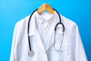 White doctor's coat with stethoscope hanging on a hanger against a blue background.
