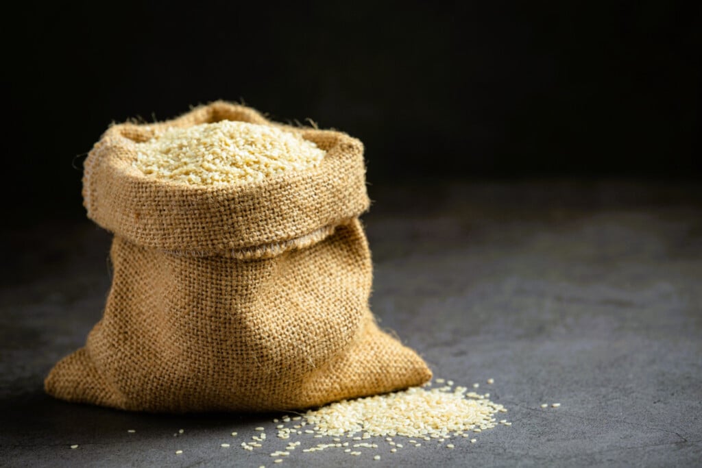 A burlap sack filled with white rice spilling onto a dark surface