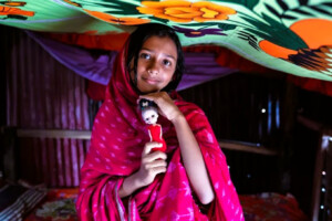 Young Bangladeshi girl in a red shawl holding a doll, symbolizing childhood amid child marriage concerns.